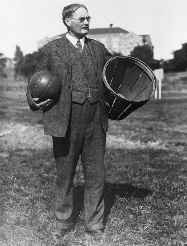 James Naismith standing with a soccer ball beside a peach-basket goal